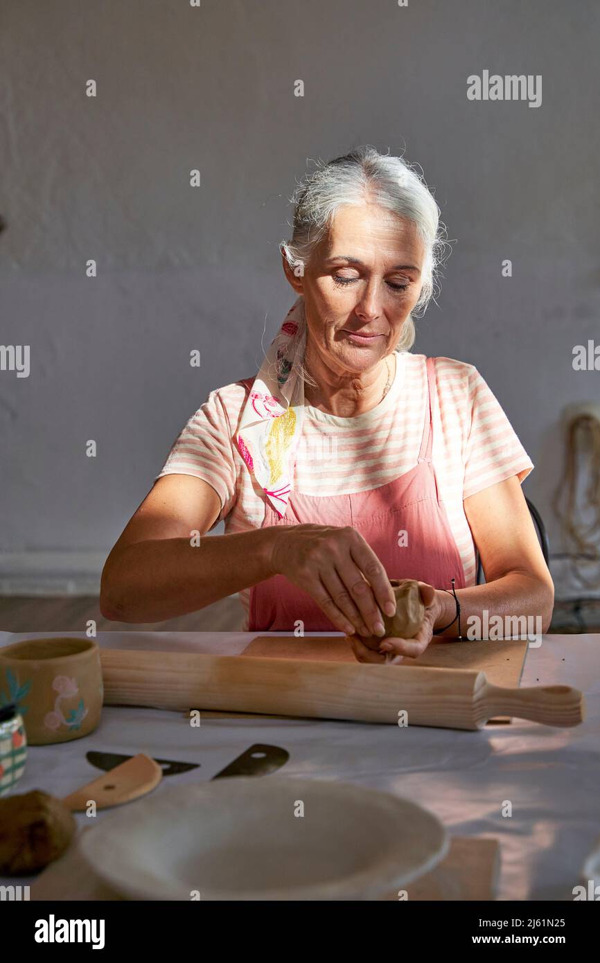Donna con capelli grigi che fanno tazza di argilla a casa Foto Stock
