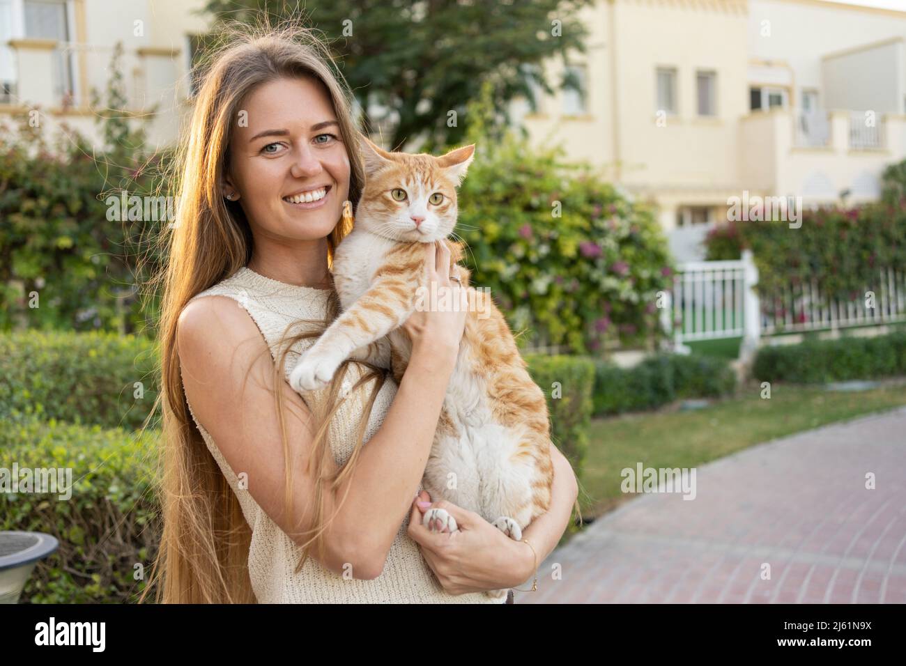 Donna felice con capelli biondi lunghi che tengono gatto zenzero in giardino Foto Stock