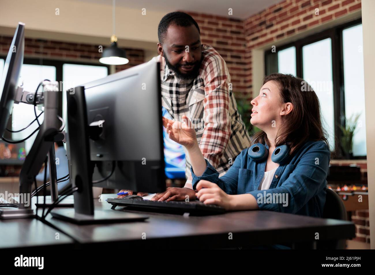 Un collega sorridente che parla con il cordiale artista 3D di arti elettroniche e grafica digitale in via di sviluppo. Agenzia creativa diversi dipendenti nel brainstorming idee di produzione. Foto Stock