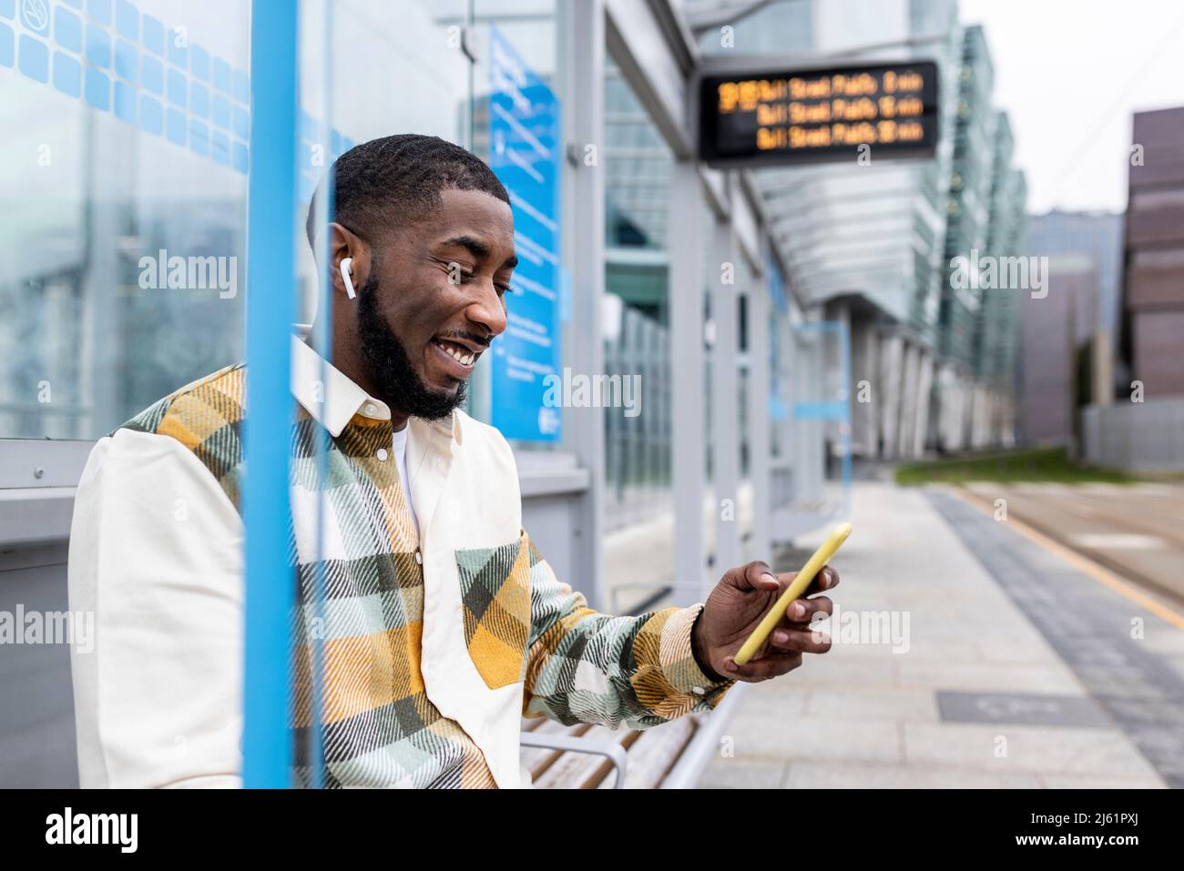 Happy man surf rete attraverso telefono cellulare seduta t stazione del tram Foto Stock