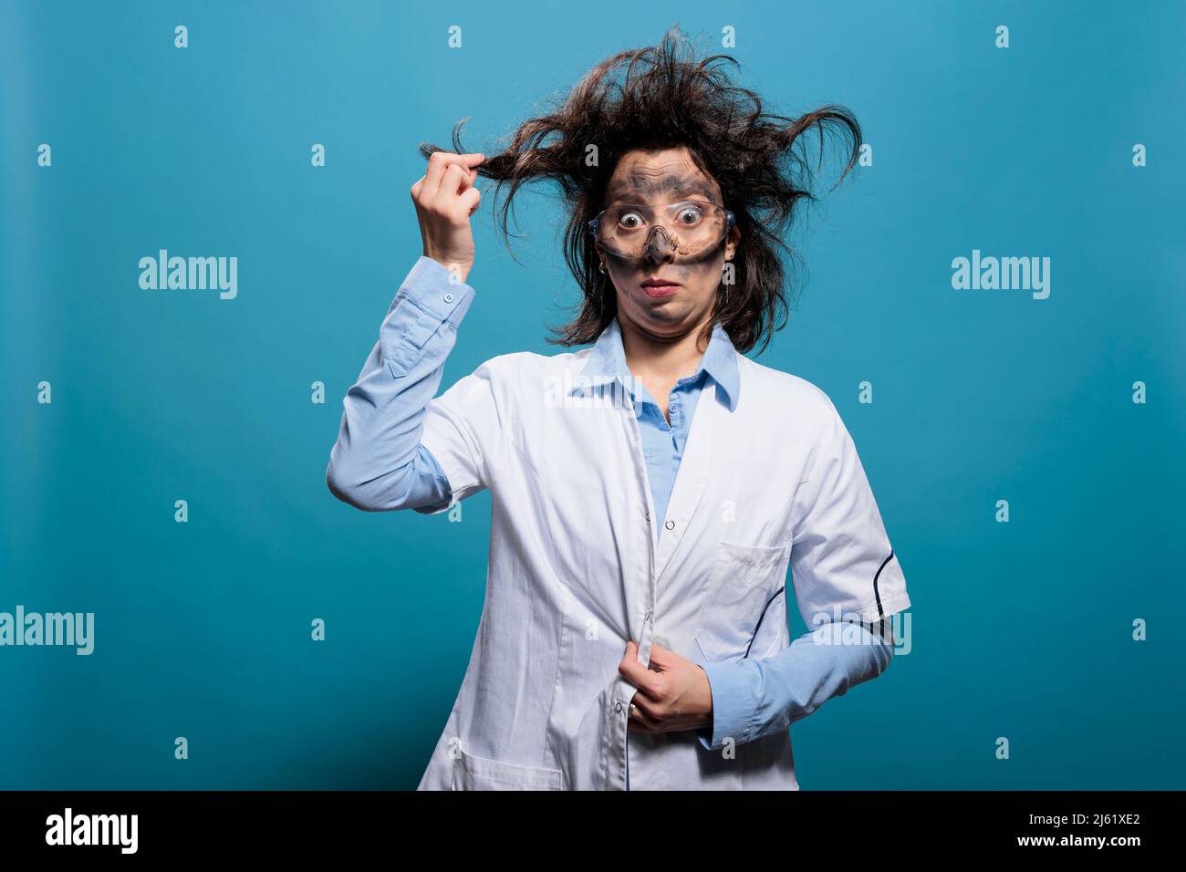 Scienziato pazzo e stravagante che afferra i capelli disordinati mentre ha faccia sporca da esplosione su sfondo blu. Insano e divertente sciocco chimico che agisce vertigini dopo esperimento chimico fallito. Foto Stock