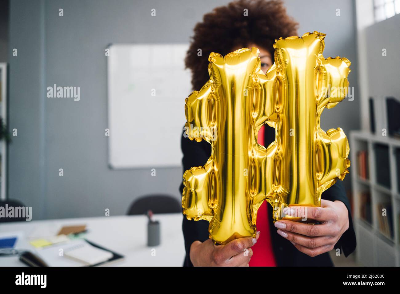 Donna d'affari con palloncino simbolo hashtag dorato davanti al viso Foto Stock