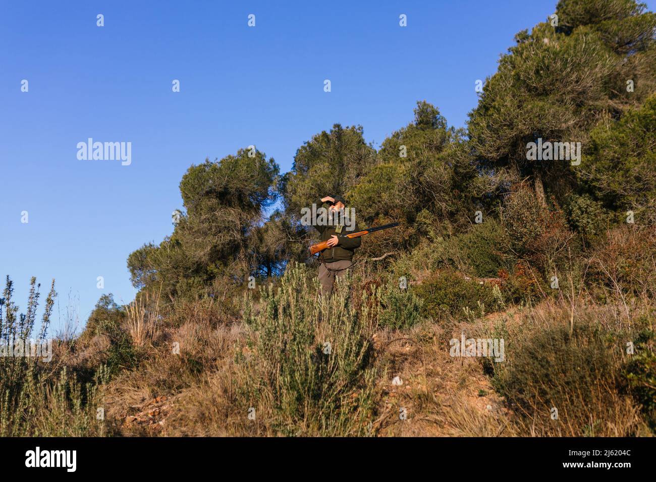 Hunter tenendo la pistola e bloccando la luce del sole con la mano mentre guarda via Foto Stock