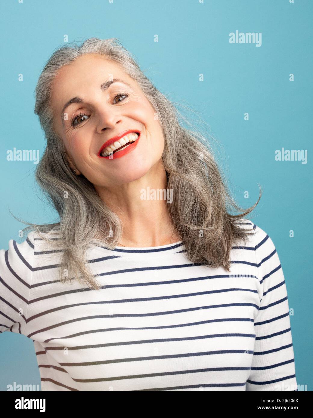 Donna felice con capelli grigi che indossano una t-shirt bianca a righe su sfondo blu Foto Stock