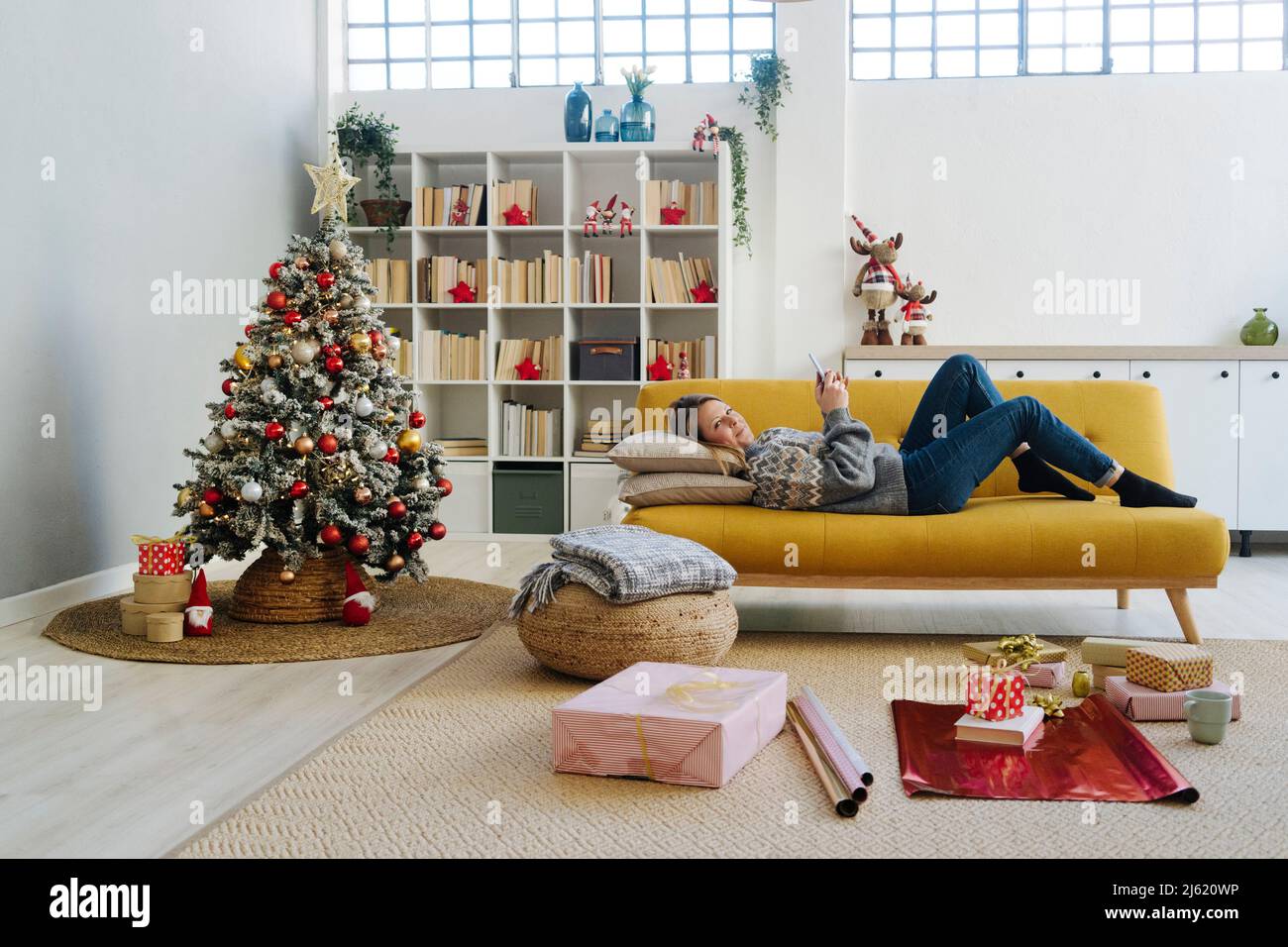 Donna con telefono cellulare sdraiato sul divano in soggiorno a casa Foto Stock