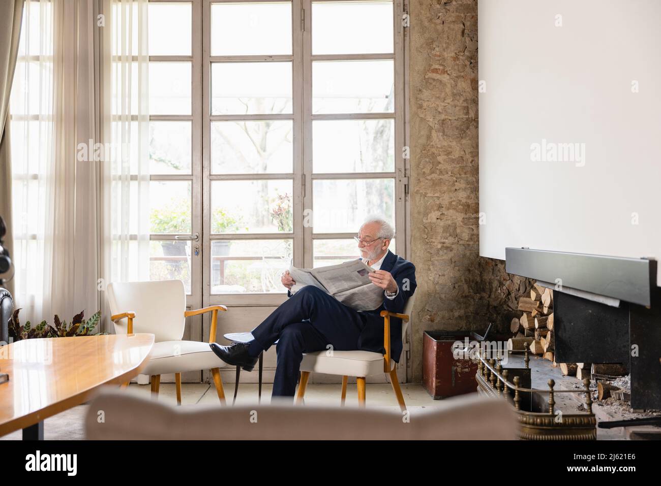 Uomo anziano che legge il giornale seduta dalla finestra nel soggiorno Foto Stock