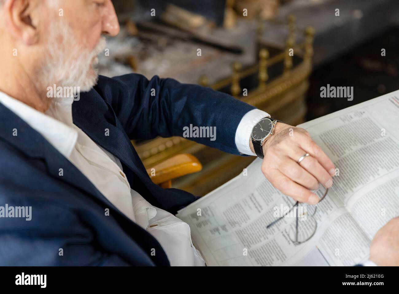 Uomo anziano con giornale che controlla l'ora seduta nel soggiorno Foto Stock
