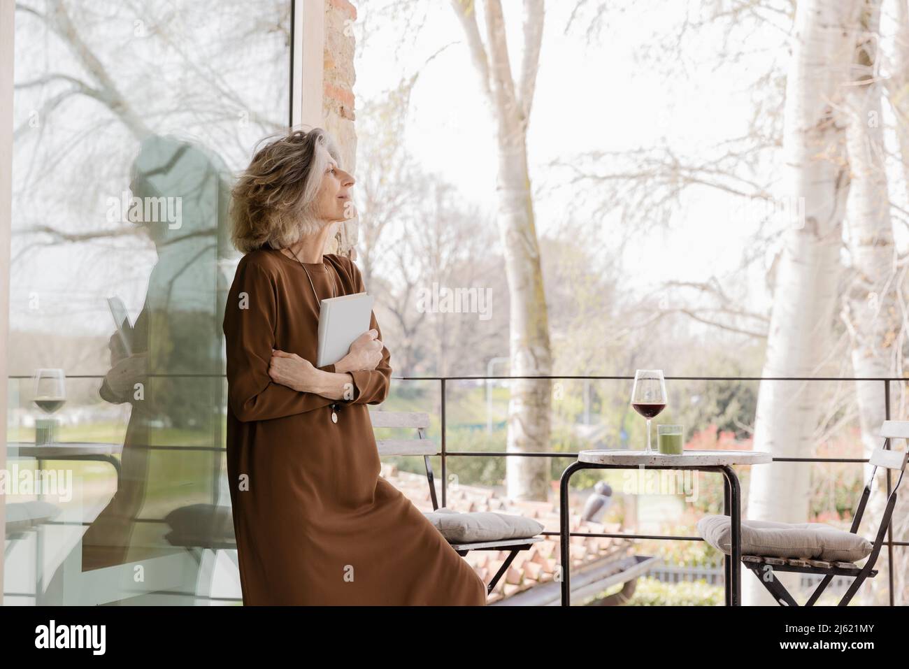 Donna anziana con libro in piedi nel balcone dell'appartamento dell'hotel Foto Stock