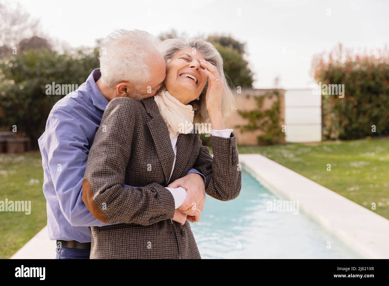 Uomo anziano che abbraccia una donna allegra di fronte alla piscina Foto Stock