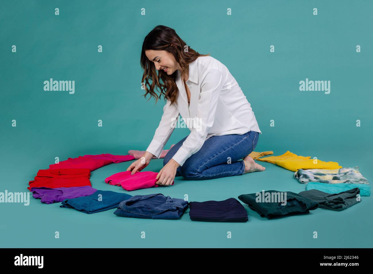 Donna sorridente che dispone t-shirt tra i vestiti su sfondo blu Foto Stock