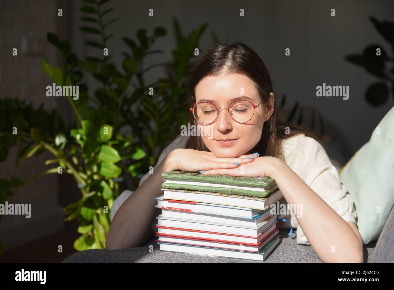Donna con occhi chiusi appoggiata sui libri a casa Foto Stock