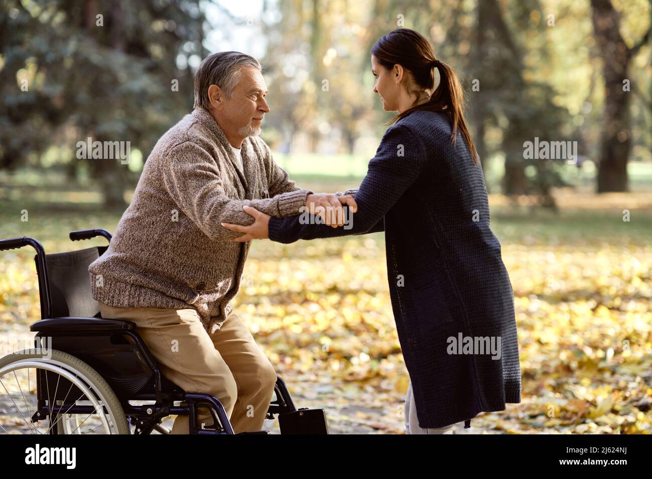 Infermiera che assiste gli anziani disabili in piedi dalla sedia a rotelle al parco Foto Stock