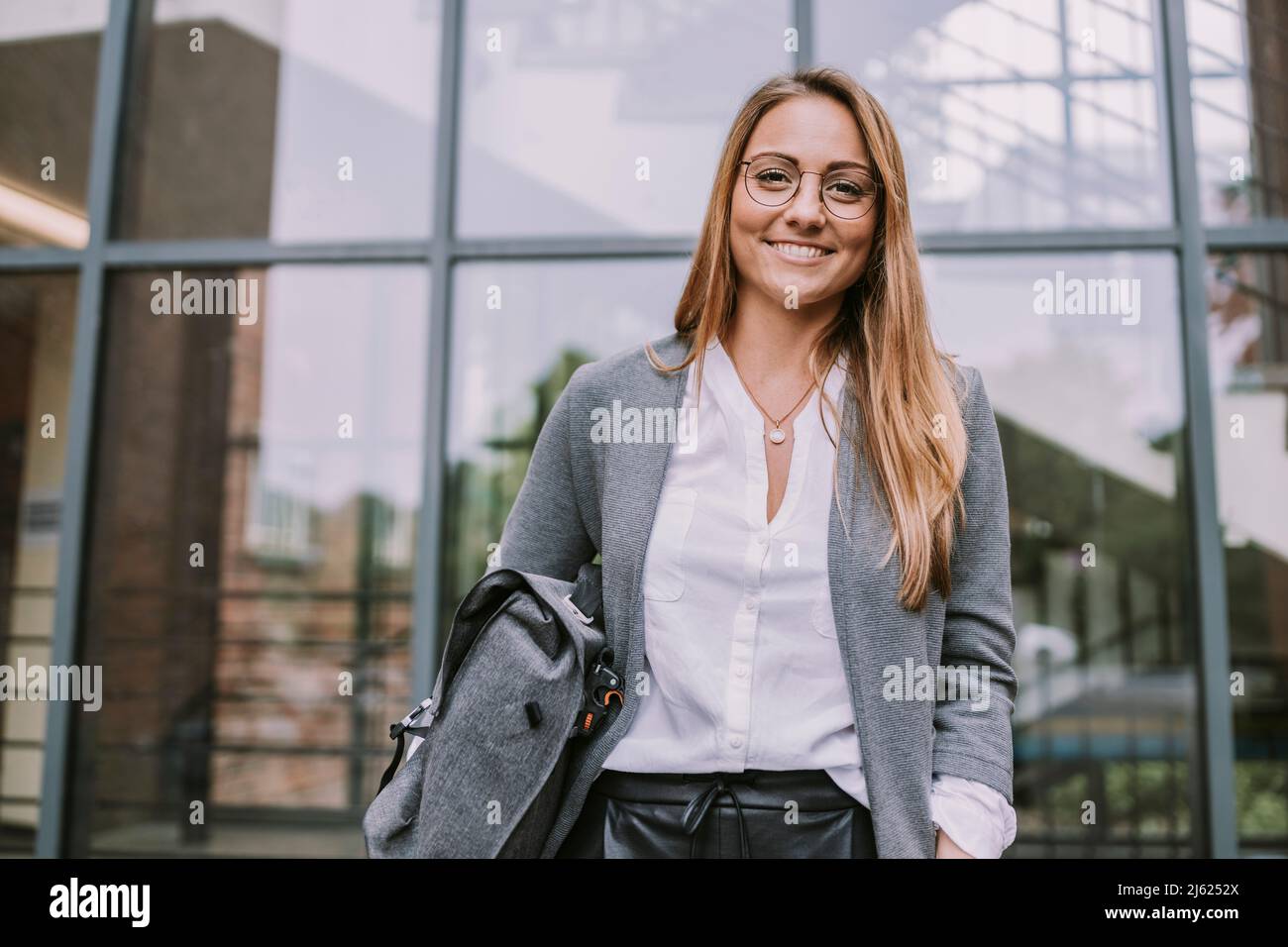 Sorridente giovane donna in piedi di fronte al muro di vetro Foto Stock