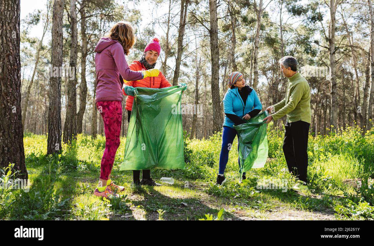 Uomini e donne maturi che raccolgono rifiuti in sacco di rifiuti in foresta Foto Stock