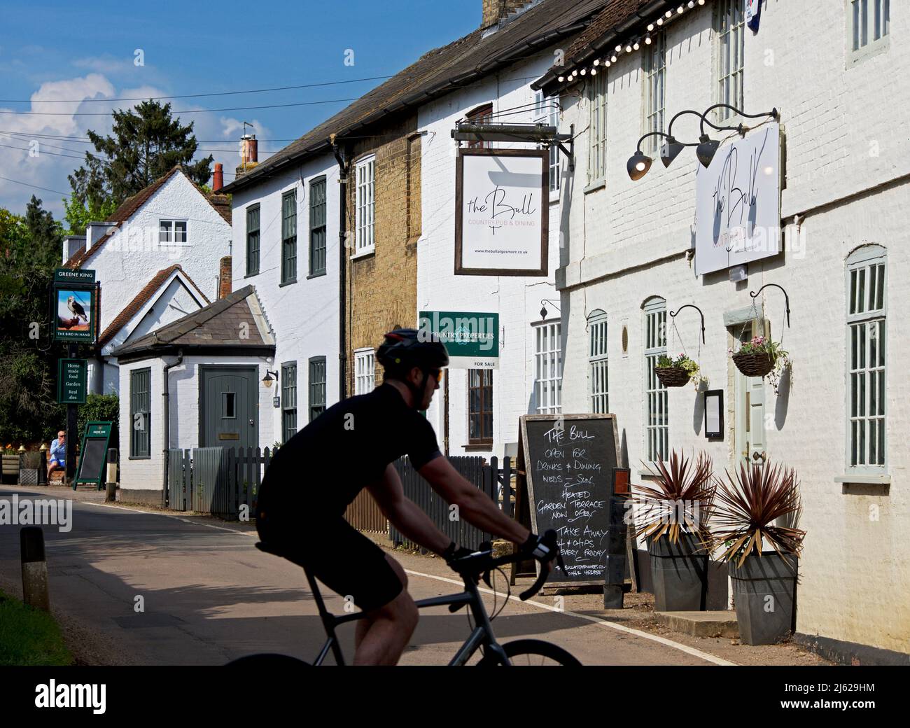Uomo in bicicletta accanto al Bull pub nel villaggio di Gosmore, Hertfordshire, Inghilterra Regno Unito Foto Stock