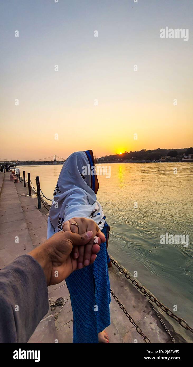 giovane coppia che tiene le mani al tramonto a ganges banca del fiume da un angolo diverso immagine è preso a ganga riva del fiume rishikesh uttrakhand india. Foto Stock