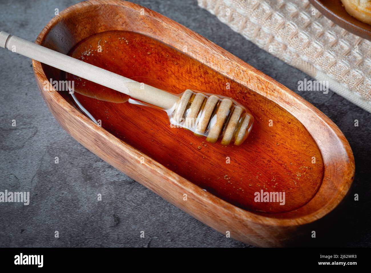 Miele in ciotola di legno con cucchiaia di miele su sfondo grigio Foto Stock