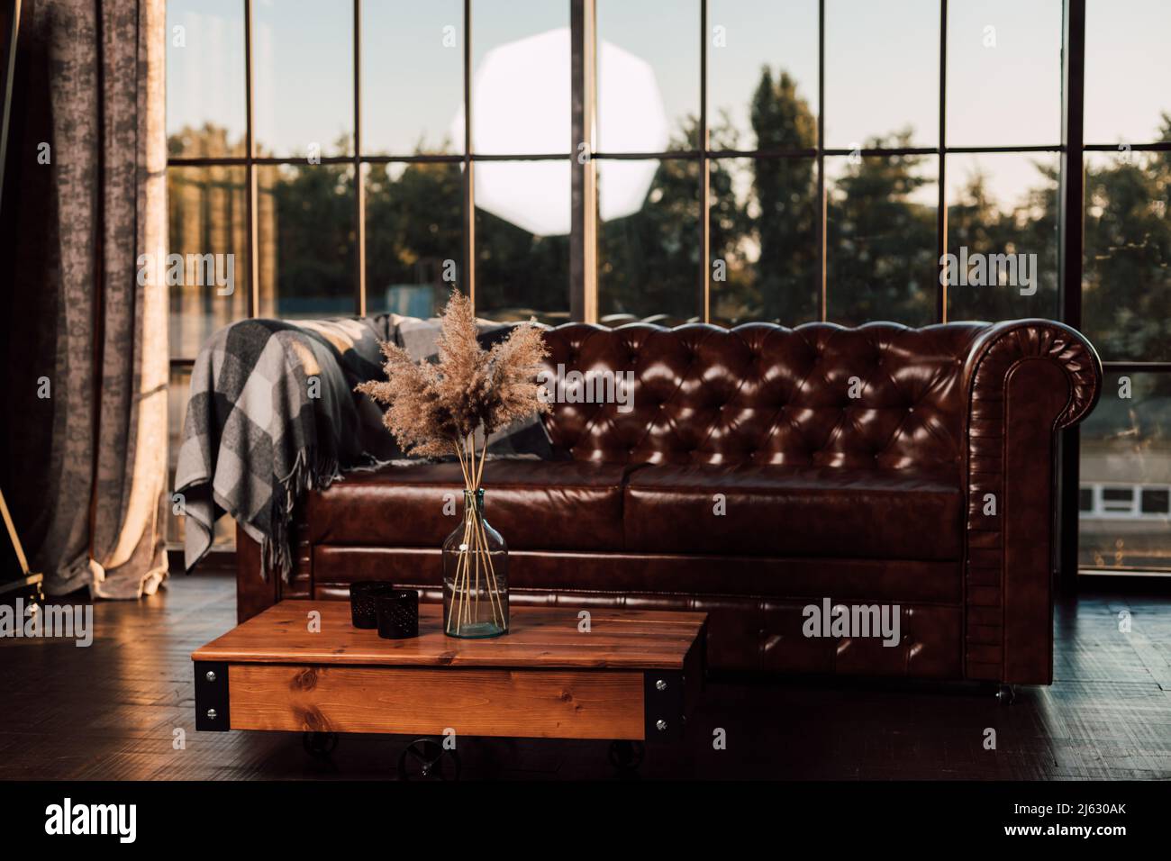 Un vaso con fiori secchi si trova su un tavolo di legno accanto al divano e alla finestra. Foto Stock