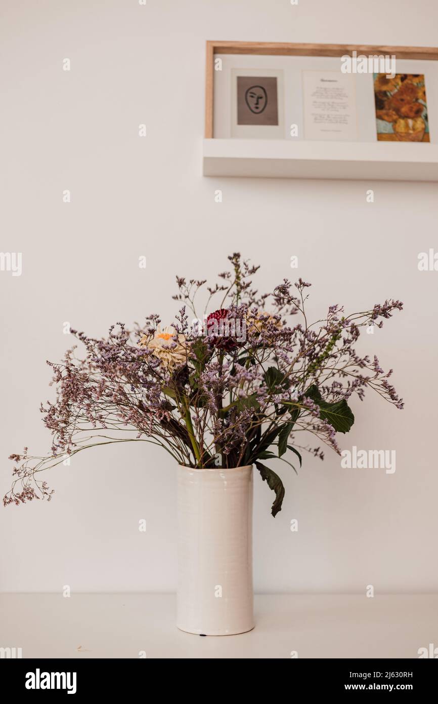 Un vaso bianco con fiori selvatici si erge su una mensola bianca all'interno Foto Stock