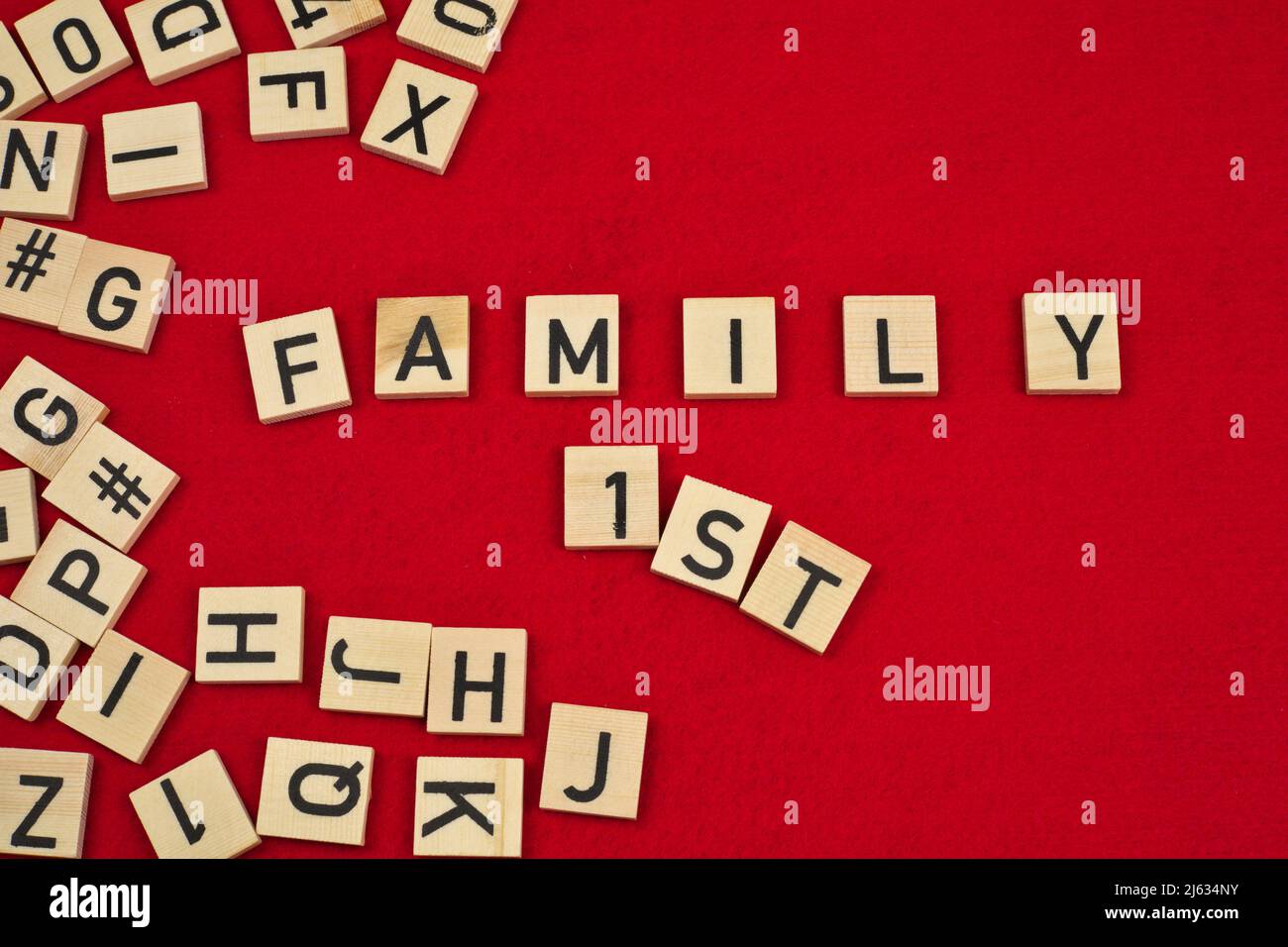 Frase 'Family 1st' su sfondo rosso feltro circondato da piastrelle di legno lettera Foto Stock