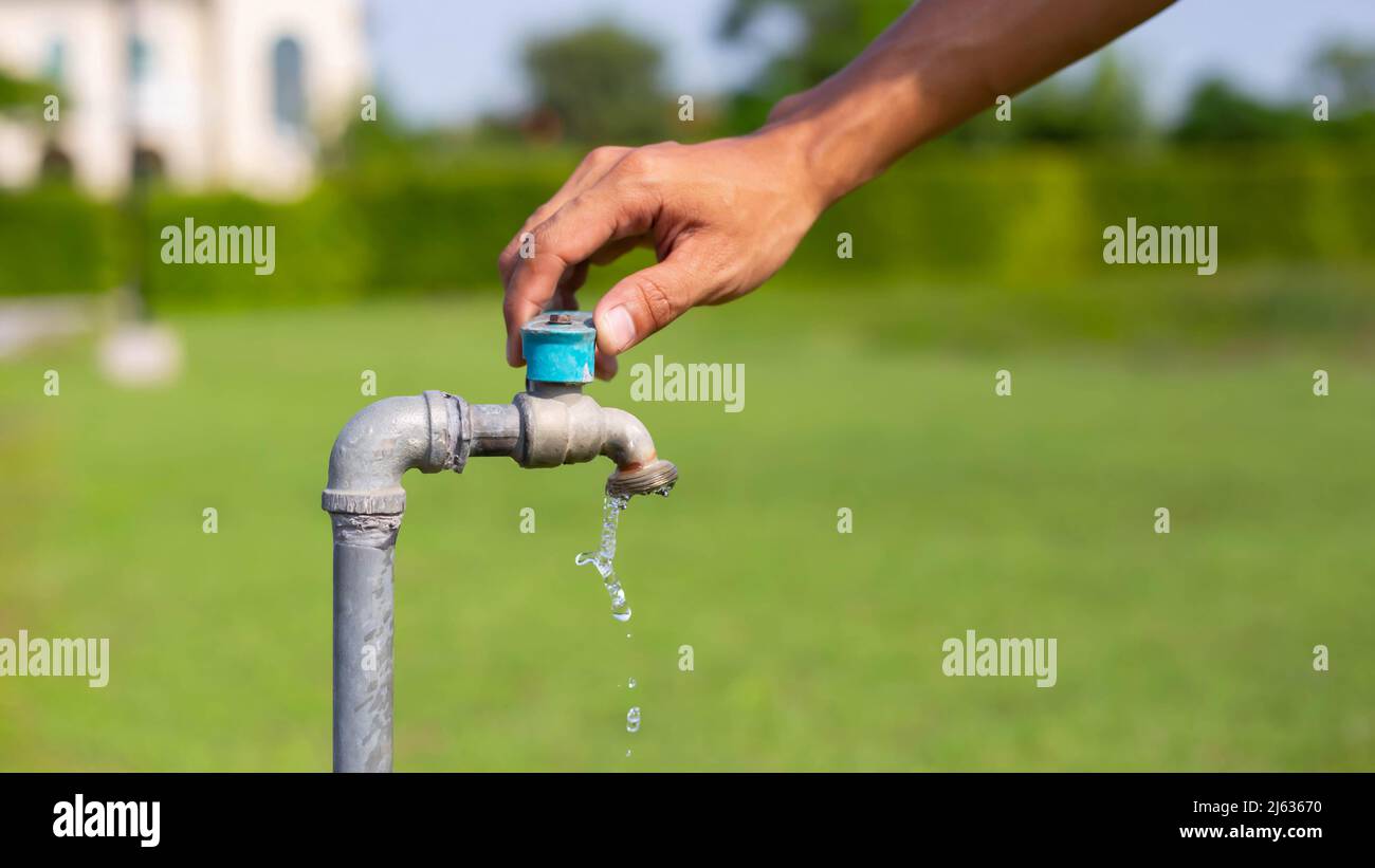 La mano maschio apre il rubinetto d'acqua del giardino, versando acqua pulita rubinetto d'acqua dolce, attivare il rubinetto, mani-fuori acqua, . Foto Stock