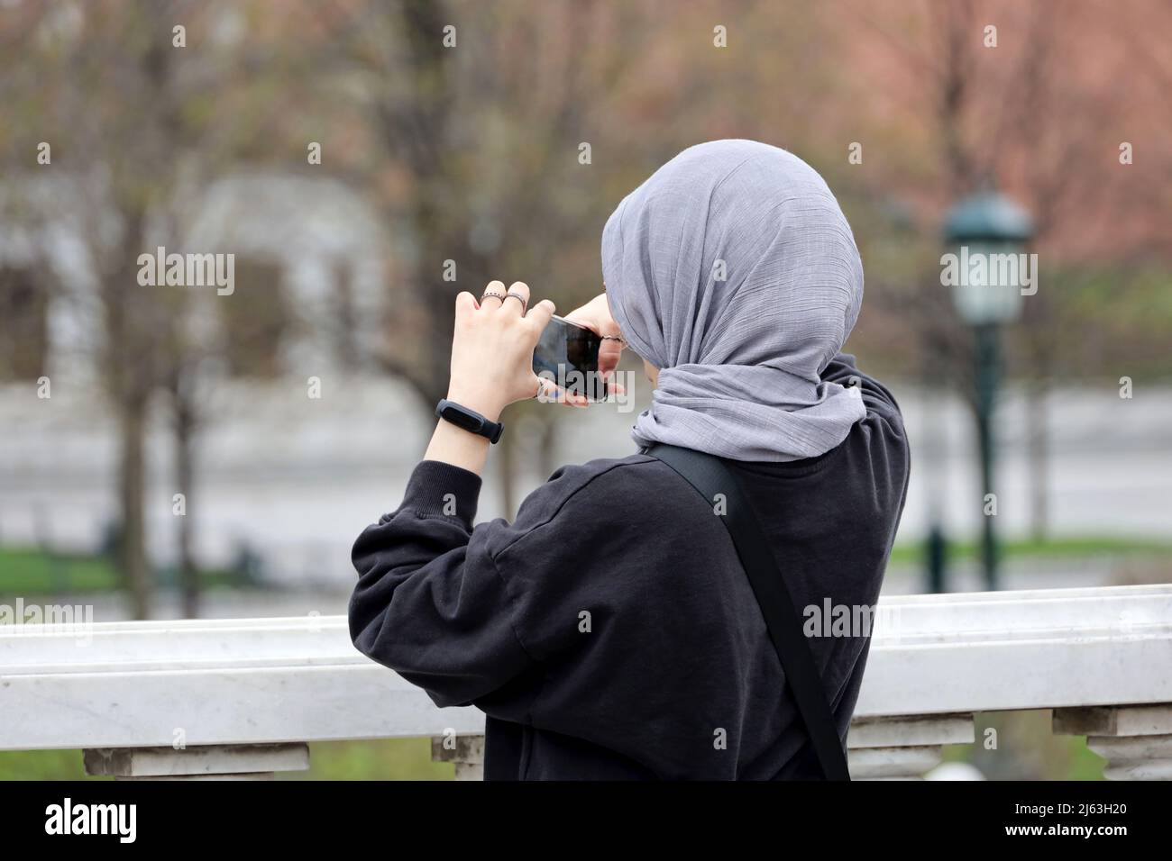 Donna musulmana che scatta foto con la fotocamera dello smartphone sulla strada della città. Ragazza in hijab in primavera parco Foto Stock