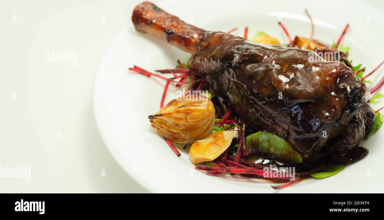 Delizioso gambo di agnello con vino rosso e salsa di rosmarino servito sull'insalata mista a foglie, piatto esclusivo Foto Stock