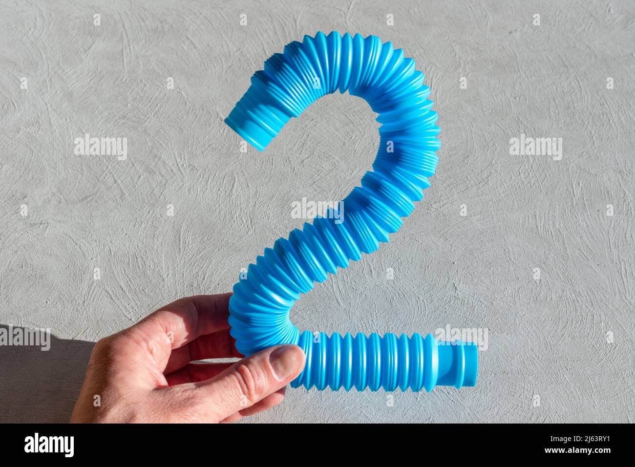 Mano femminile che tiene un tubo pop sensoriale anti-stress su sfondo bianco. Tubo corrugato flessibile su sfondo bianco. Gioco per lo sviluppo di Foto Stock