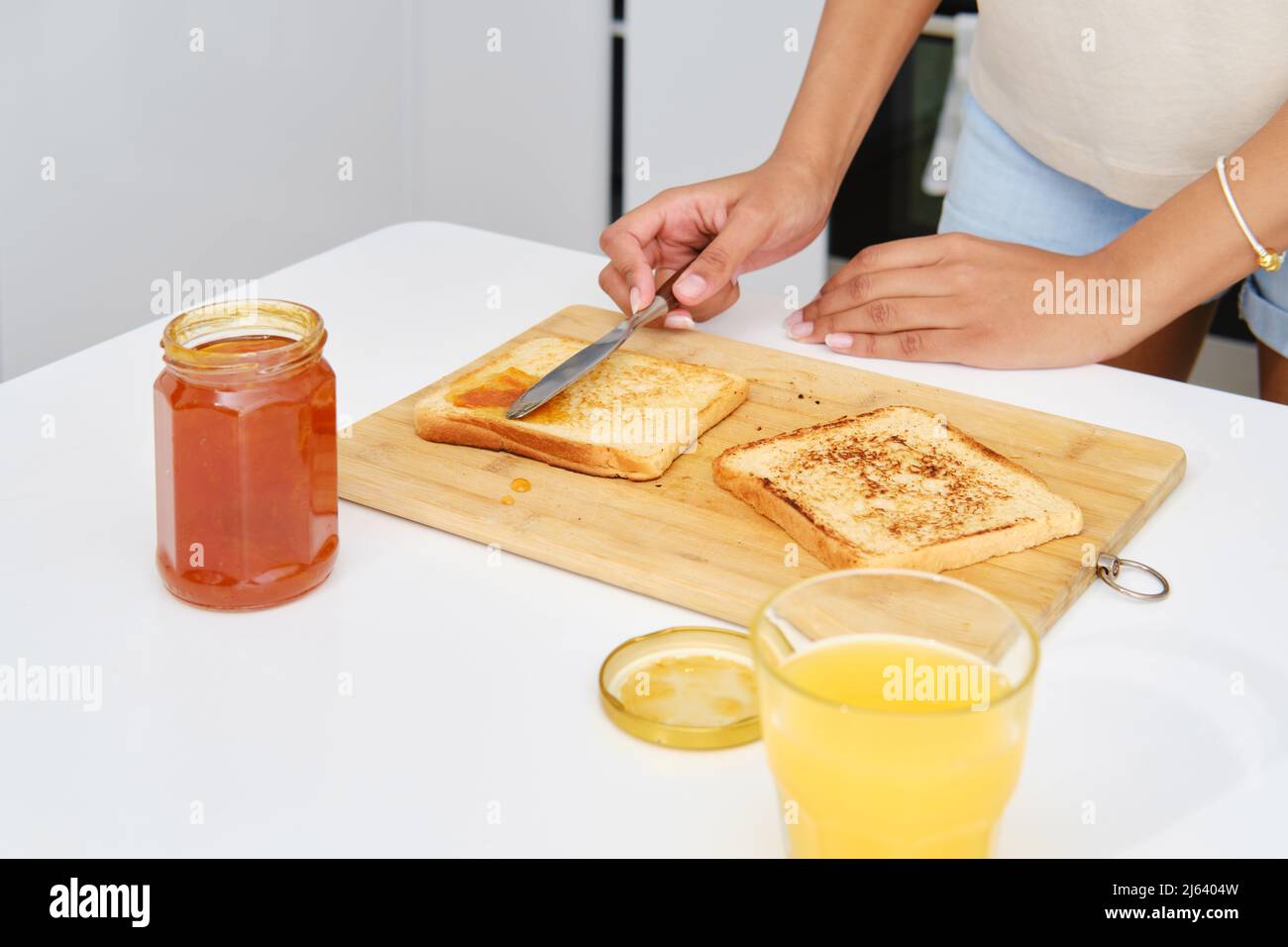 Primo piano delle mani femminili che spalmano gustose marmellate di albicocche su una fetta di pane tostato Foto Stock