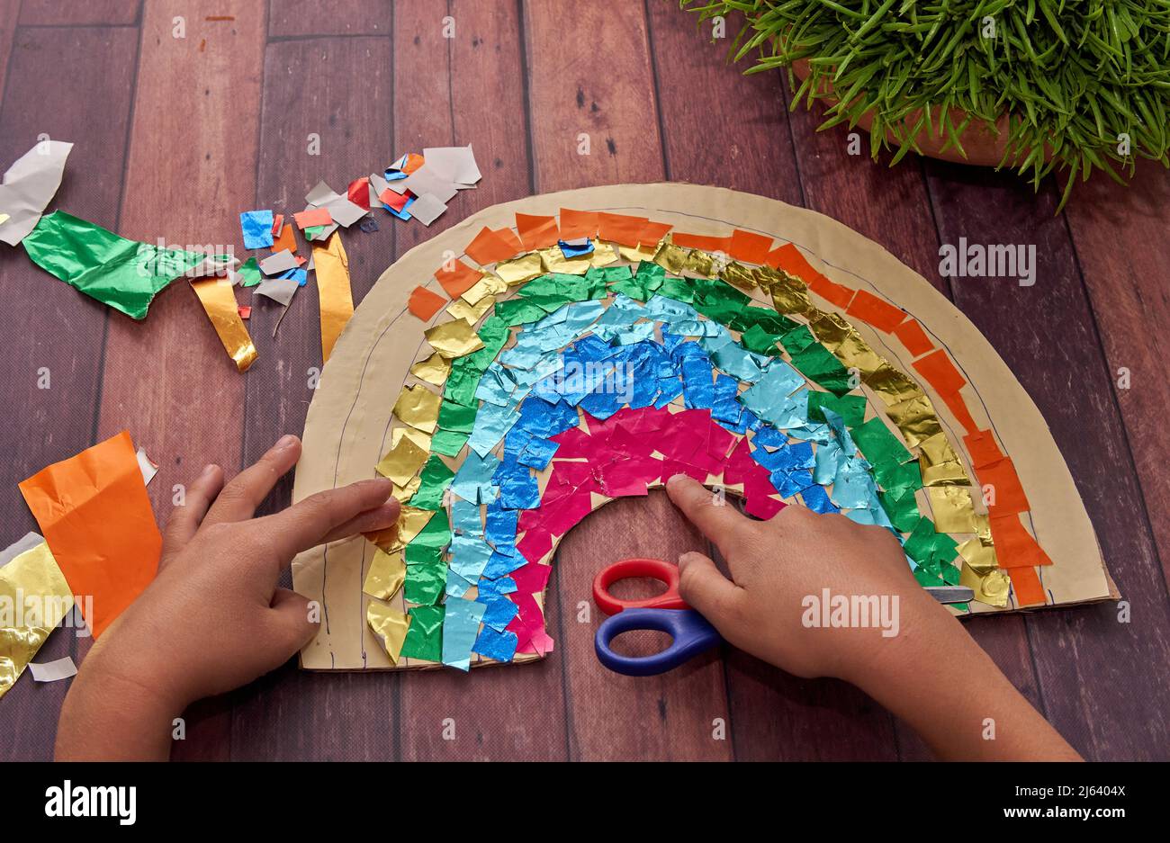le mani del bambino fanno un arcobaleno con carta colorata e una forbice su un tavolo di legno per celebrare la primavera. orizzontale. Attività per bambini a casa Foto Stock