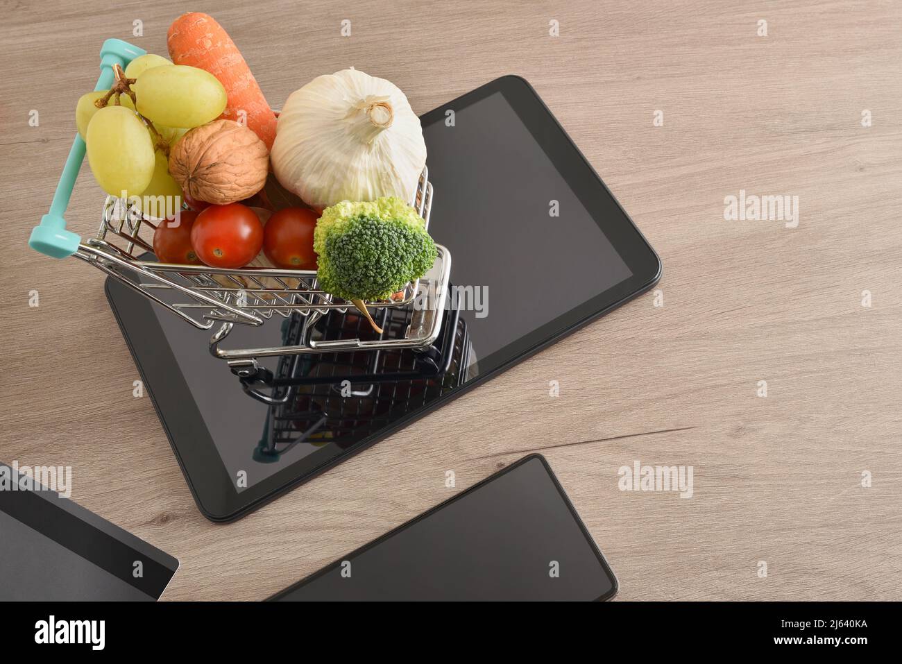 Shopping online background con dispositivi mobili e mini supermercato carrello pieno di frutta e verdura su tavola di legno. Vista dall'alto. Orizzontale Foto Stock