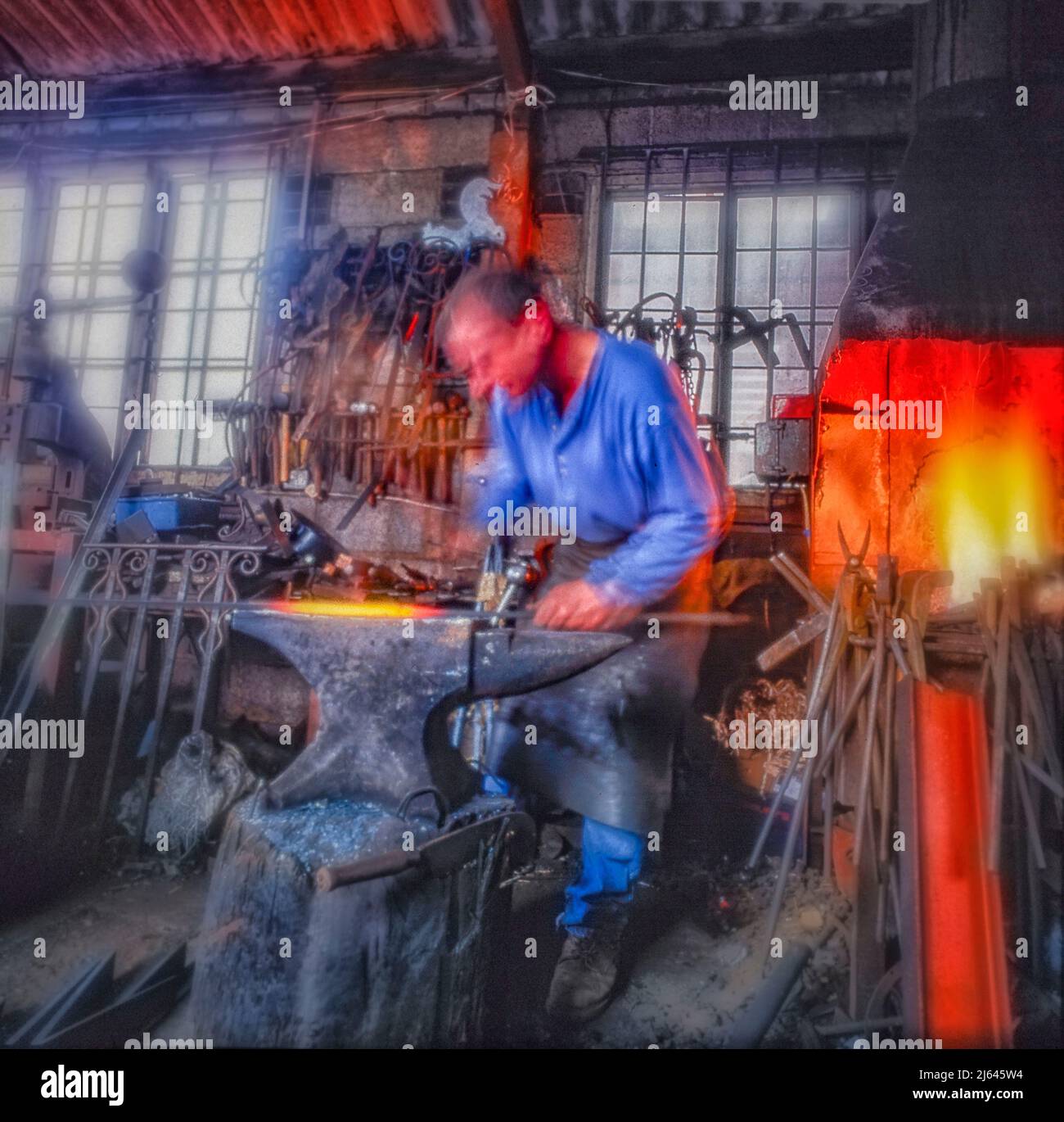 Blacksmith tradizionale che lavora al suo incudine con fiamme sullo sfondo Foto Stock