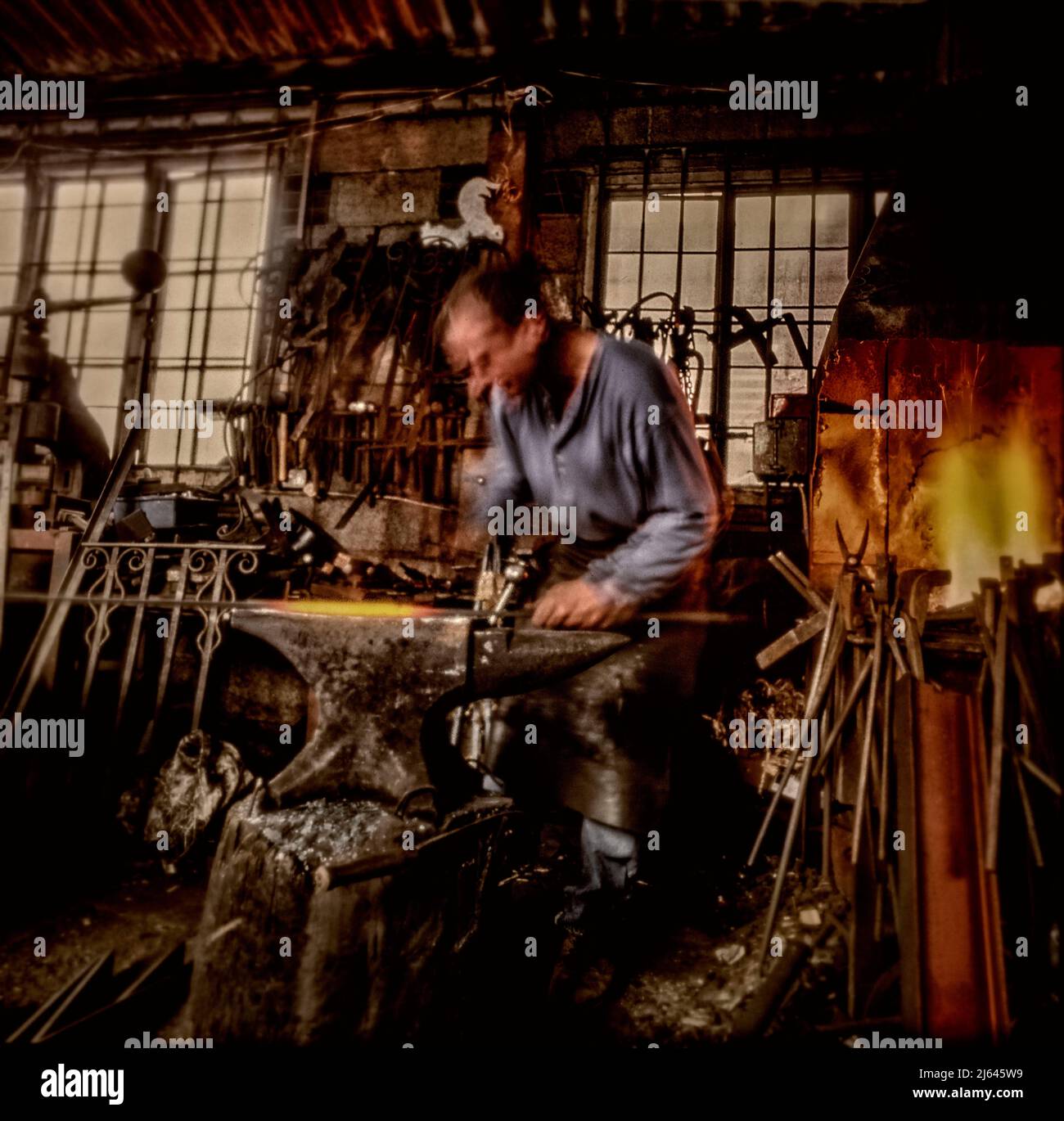 Blacksmith tradizionale che lavora al suo incudine con fiamme sullo sfondo Foto Stock