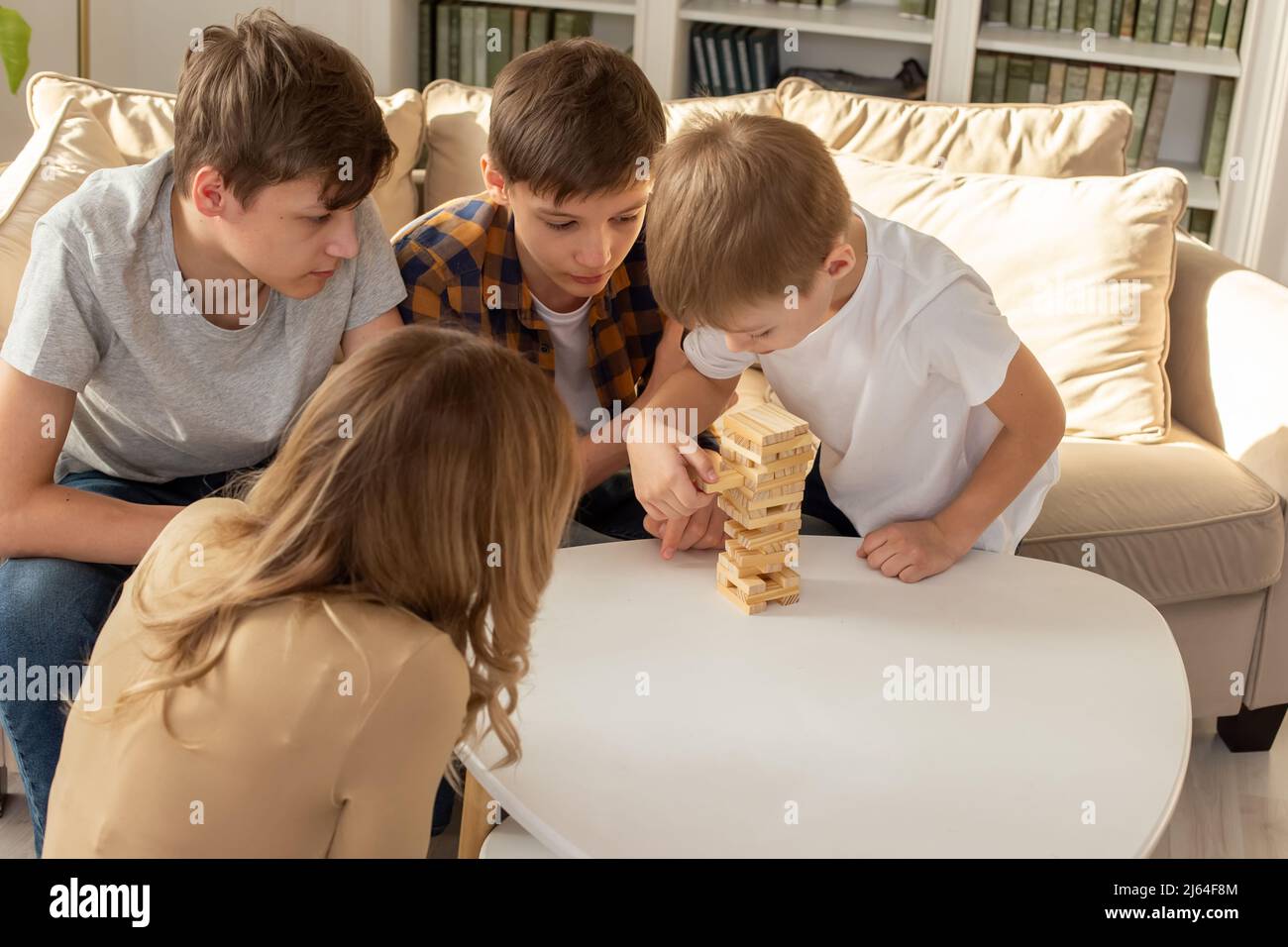 Una donna e tre ragazzi stanno giocando con entusiasmo un gioco da tavolo fatto di blocchi rettangolari di legno Foto Stock