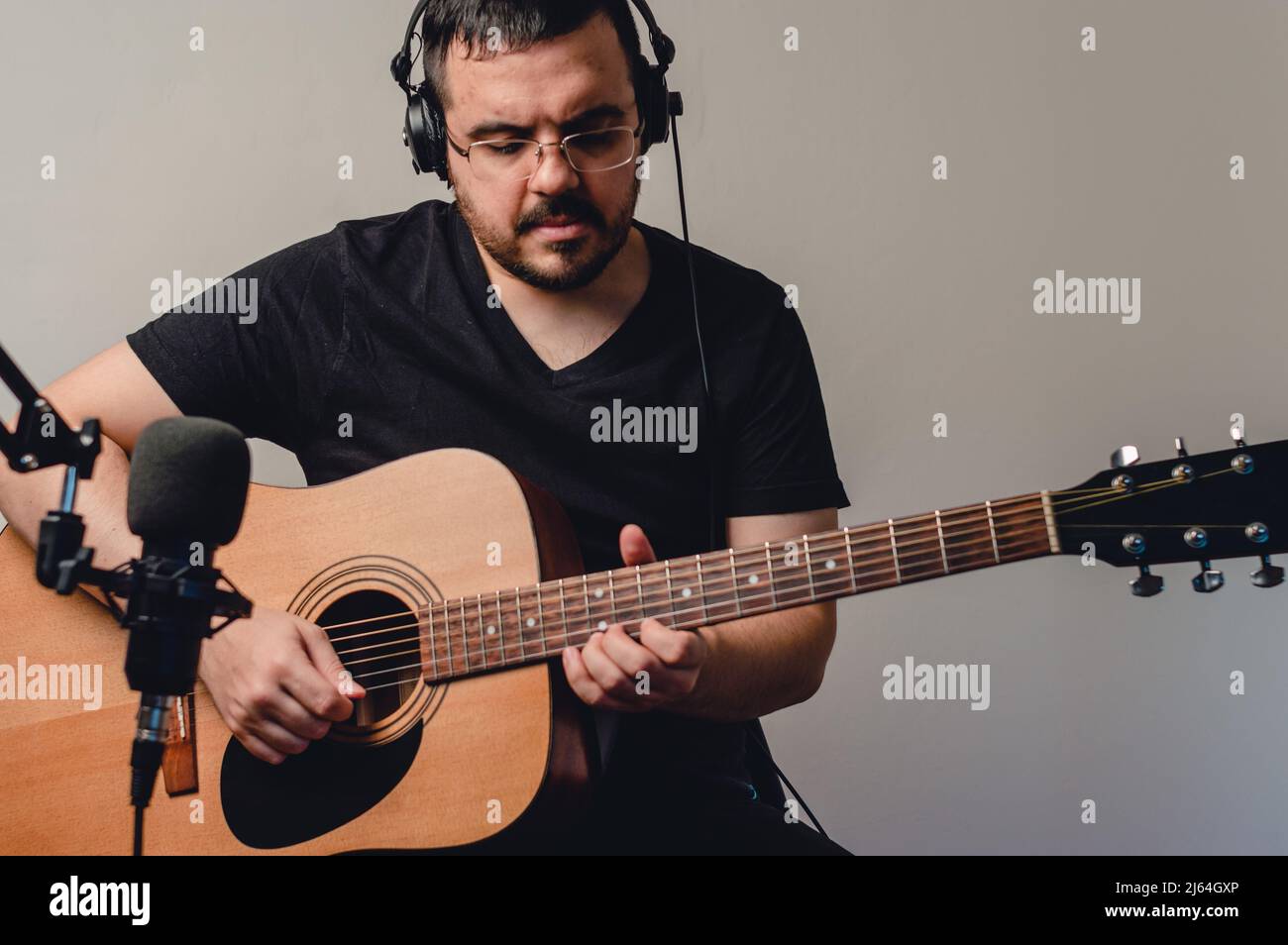 ritratto giovane uomo caucasico con cuffie registrazione chitarra acustica in casa studio, con microfono a condensatore, vista frontale, spazio copia. musica indust Foto Stock