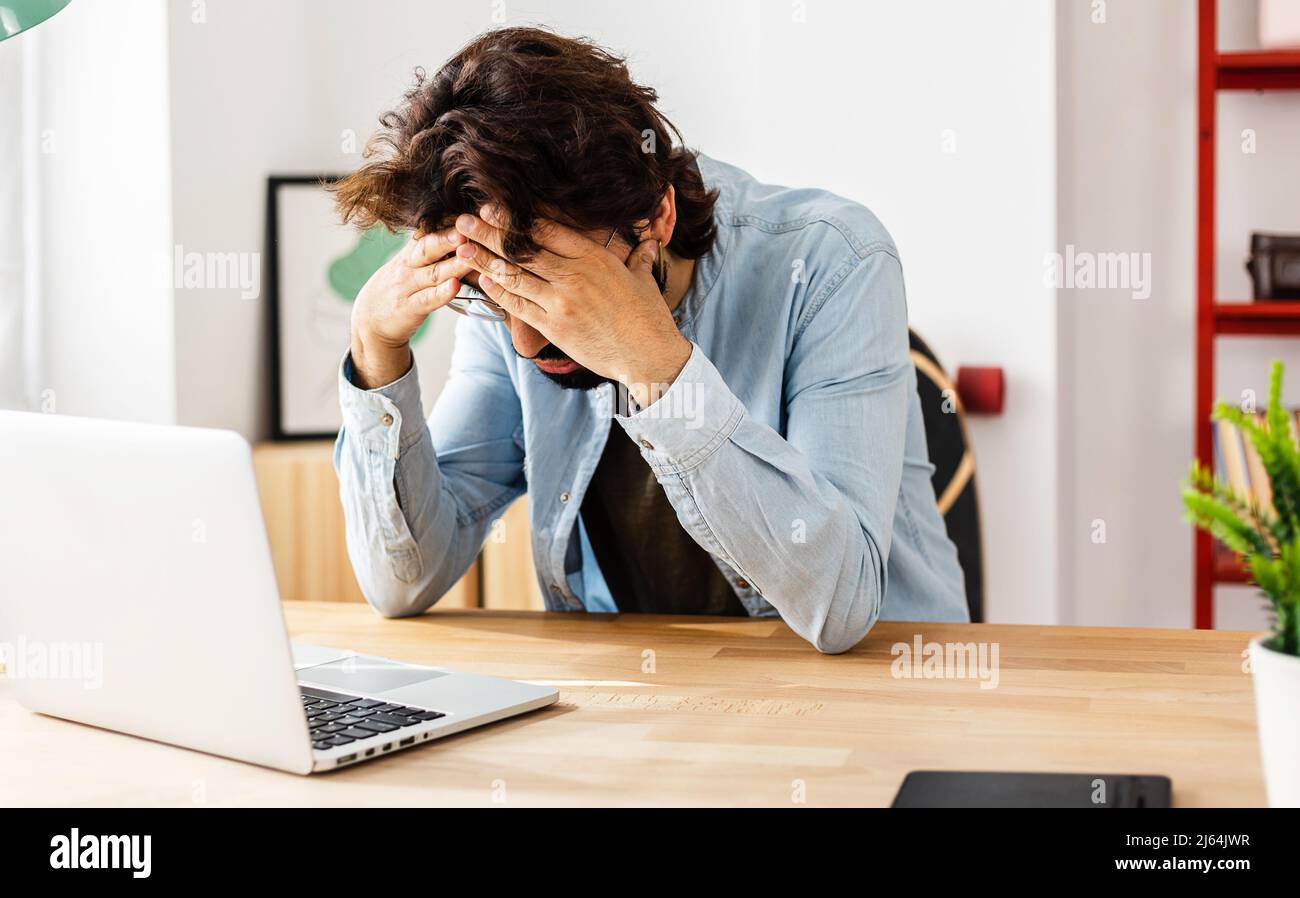 Uomo stressato con un computer portatile seduto sulla scrivania dell'ufficio a casa Foto Stock
