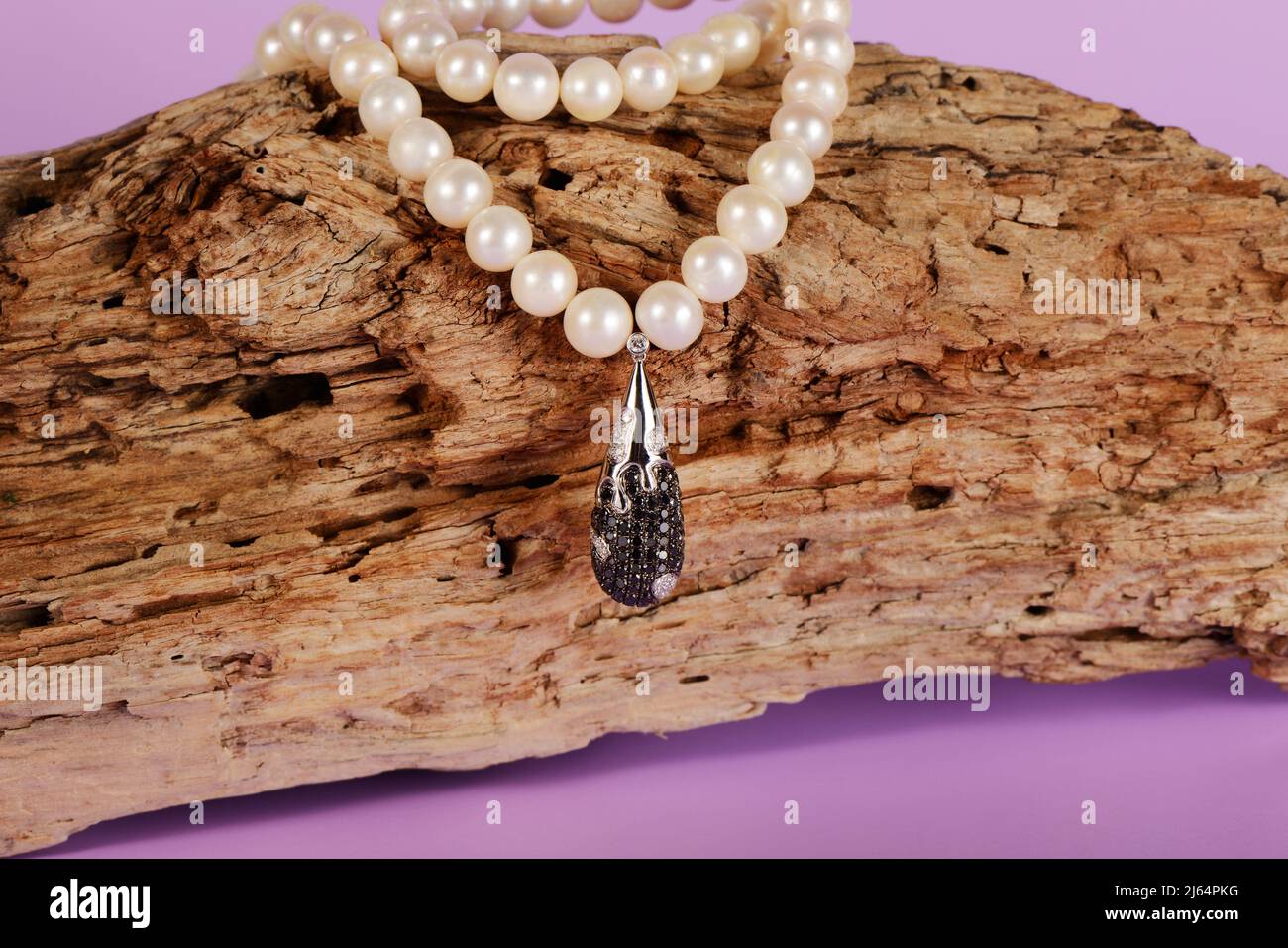 Pendente da donna in platino con diamanti bianchi e neri su una collana di perle di pregio, primo piano. Vecchio sfondo di legno. Gioielli femminili di lusso Foto Stock