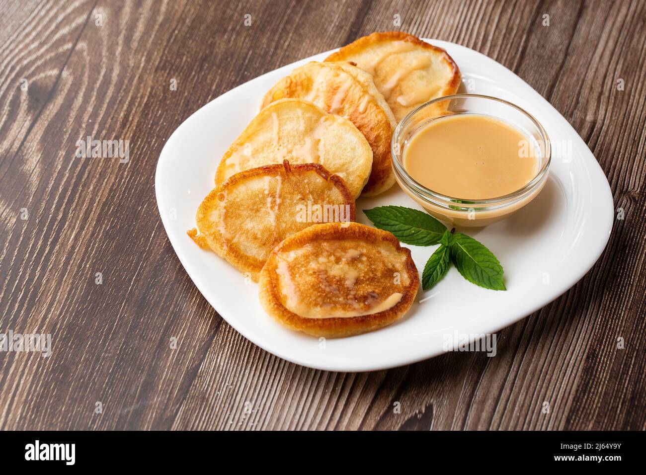 Mucchio di frittelle spesse fritte di fresco, nelle cucine dell'Europa orientale chiamate oladky o oladyi con latte condensato su sfondo di legno. Foto Stock