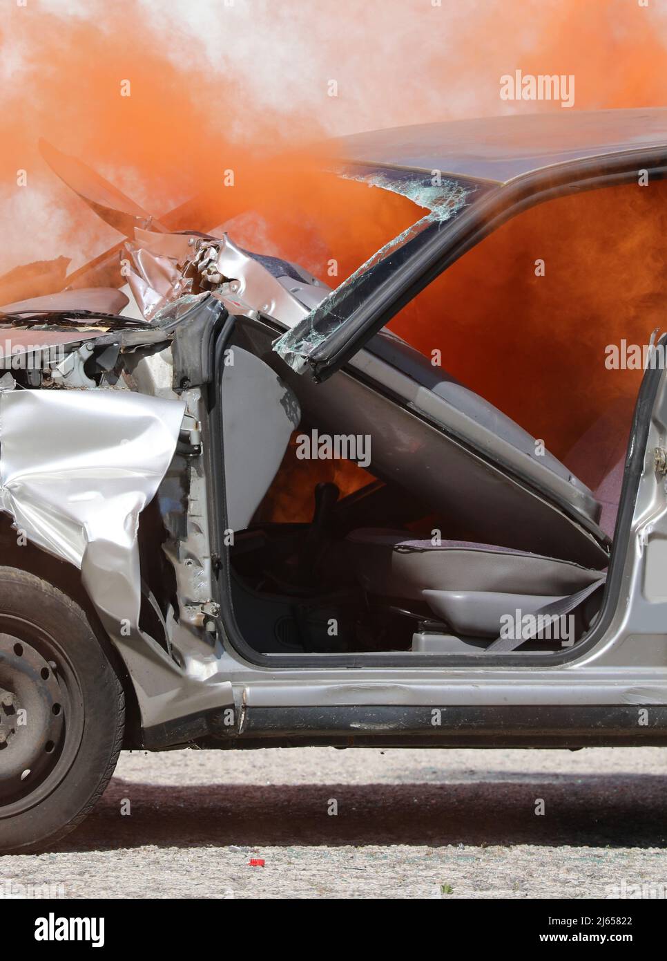il fumo arancione spesso che esce dalla macchina schiantata completamente distrutto dopo l'incidente stradale sulla strada Foto Stock