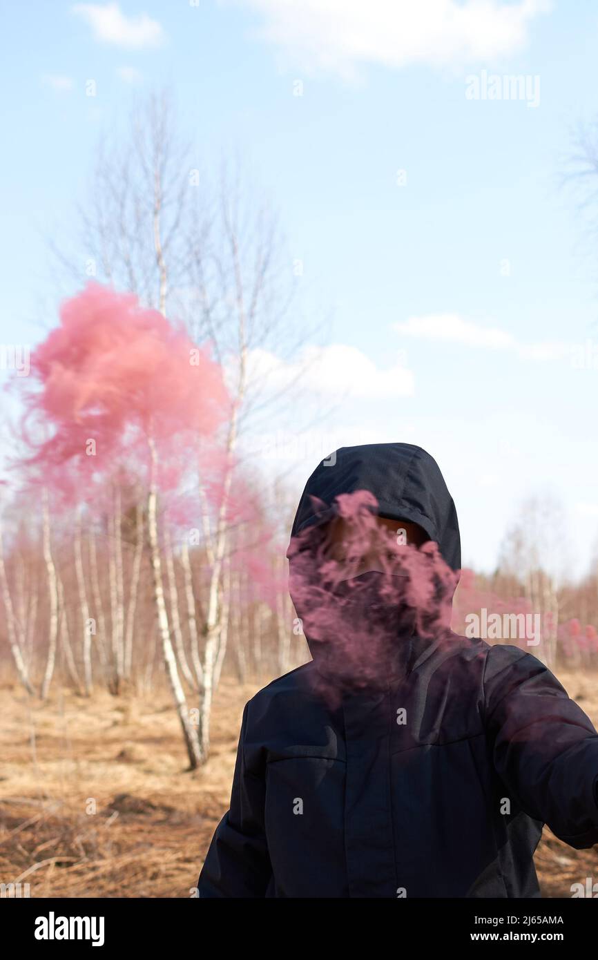 Un preteen in una giacca nera e una maschera tiene una scacchiera con fumo colorato Foto Stock