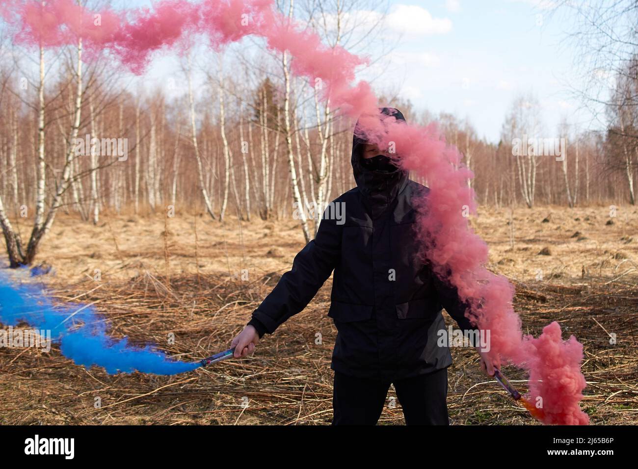 Un presepee in una giacca nera e una maschera contiene due bombe fumogene colorate Foto Stock