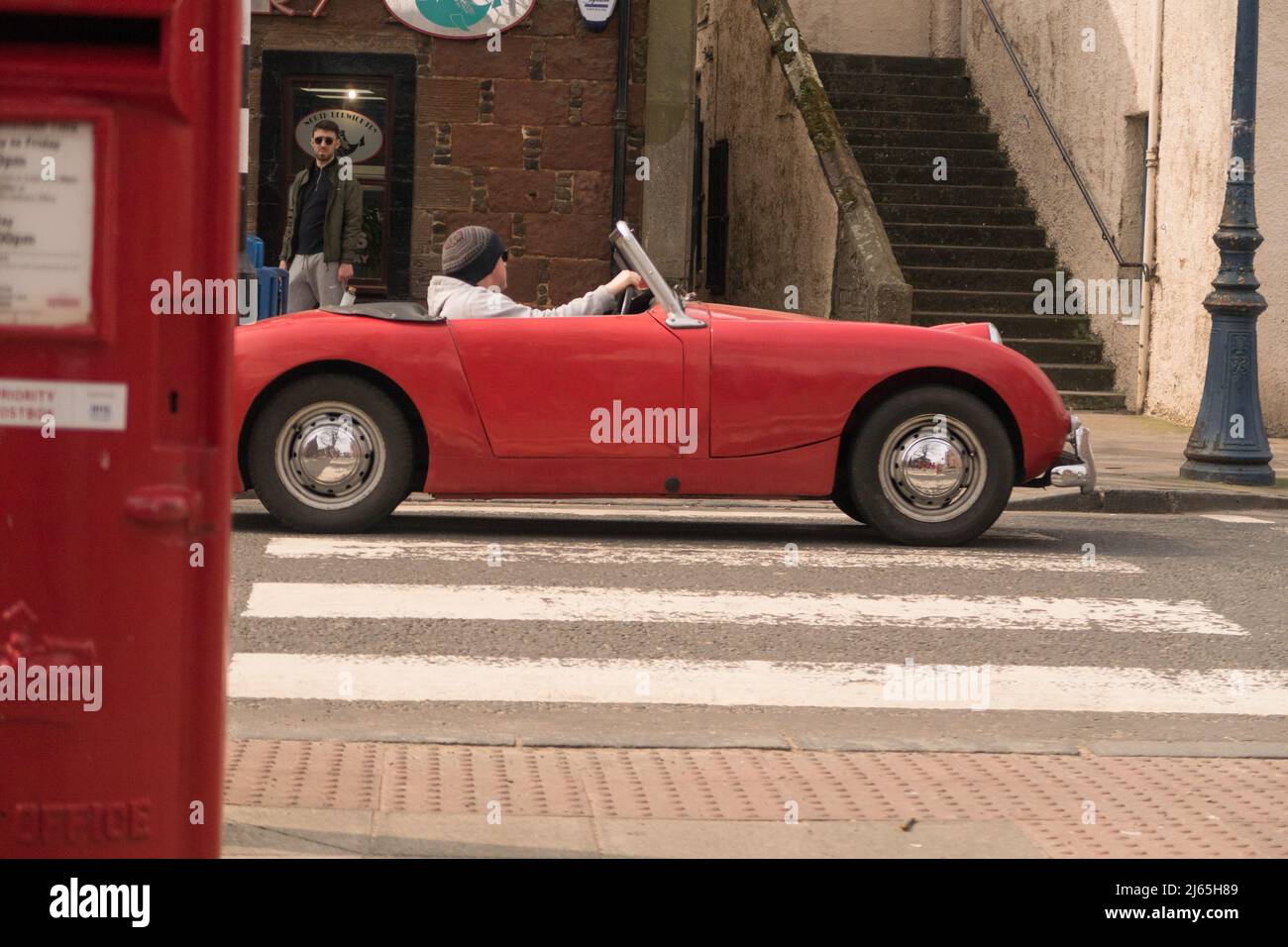 Un'auto rossa convertibile Austin Healey Sprite che attraversa un villaggio in Scozia. Foto Stock