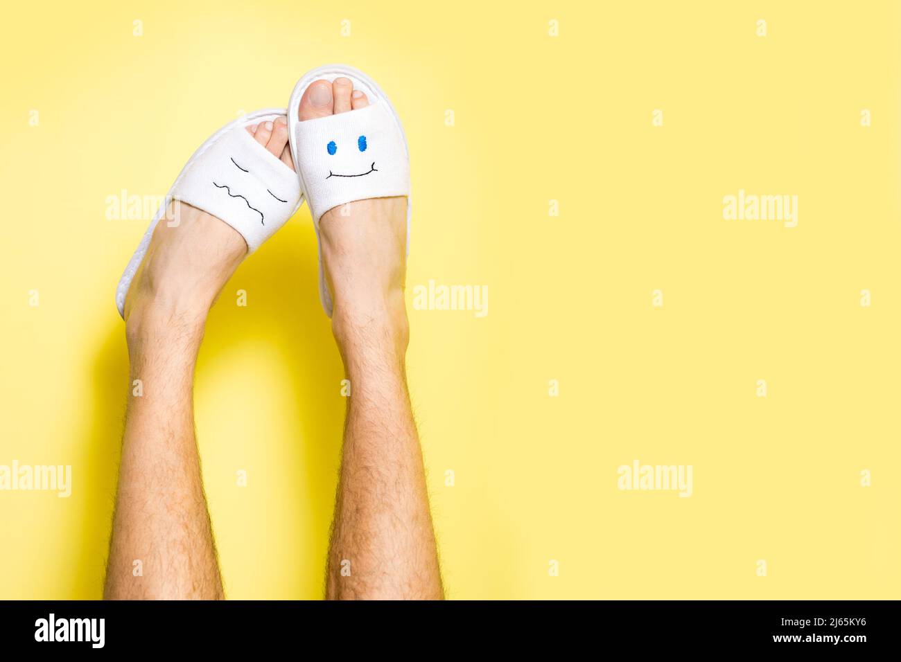 Gambe maschili che indossano pantofole divertenti con i volti Foto Stock