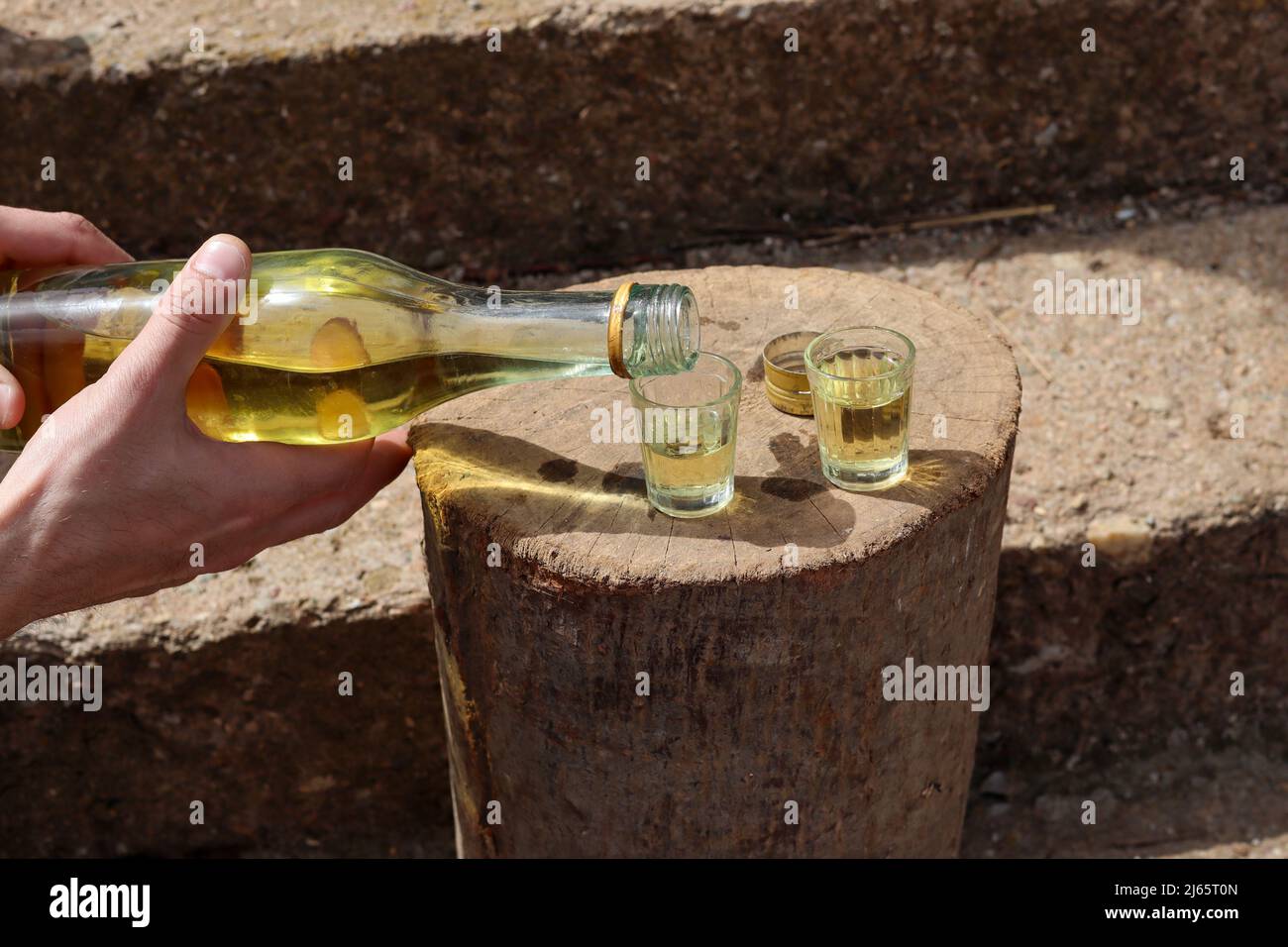 Un uomo versa il tradizionale brandy serbo chiamato rakija in un piccolo vetro speciale all'aperto su un ceppo di legno Foto Stock