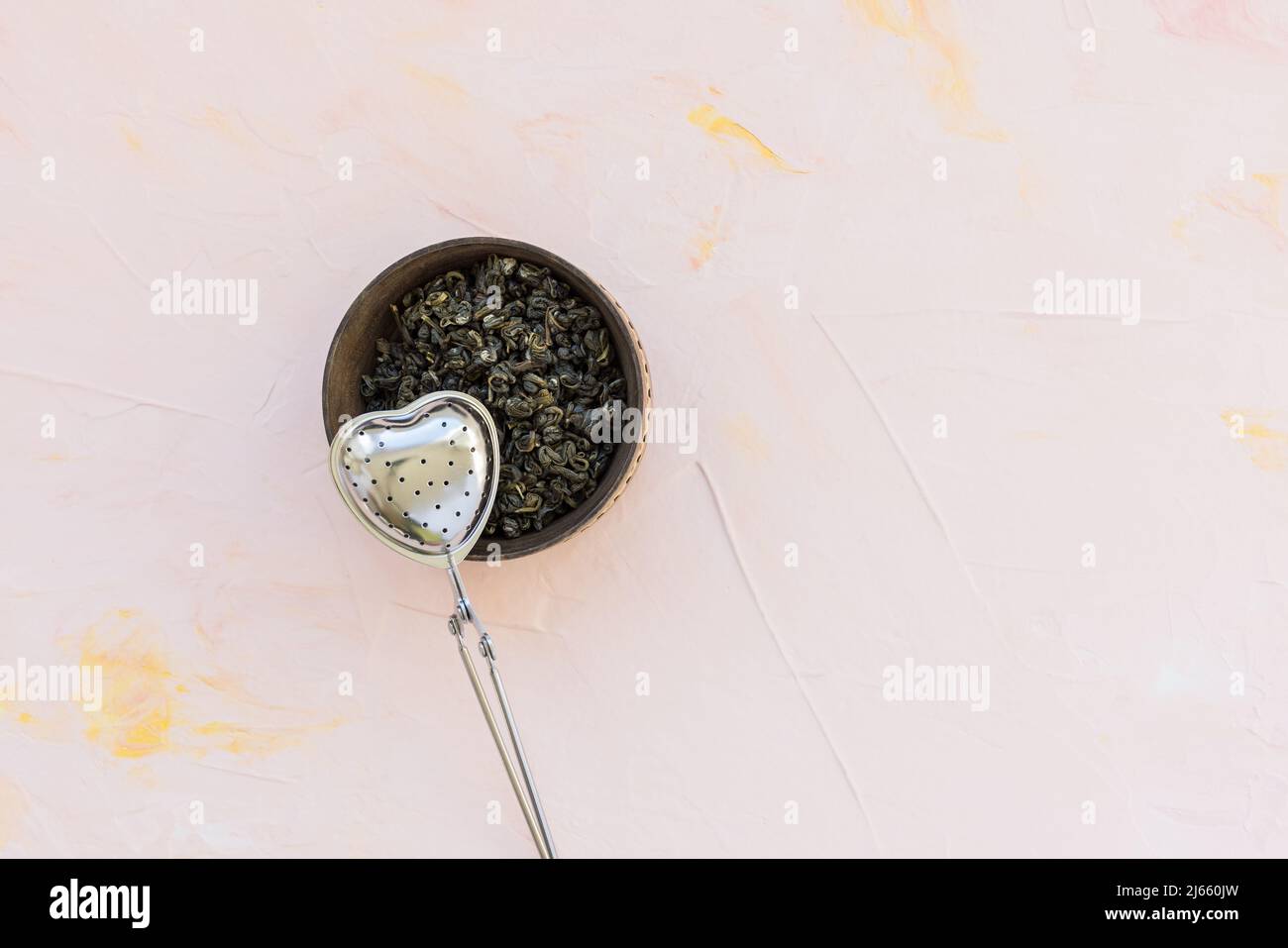 Tè cinese in foglie sciolte di alta qualità. Foglie di tè verde Jasmine rotolate a spirale stretta. Palline di tè verde lumaca in ciotola di legno su sfondo rosa. Dragon Pearl Jasmine sfere di tè verde lumaca e tè più ripido sullo sfondo. Vista dall'alto, spazio di copia Foto Stock