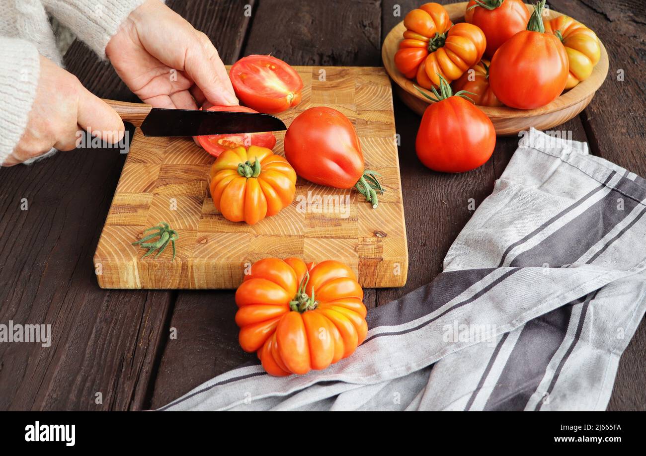 Pomodori freschi maturi e coltello su tavola rustica di legno su sfondo scuro Foto Stock