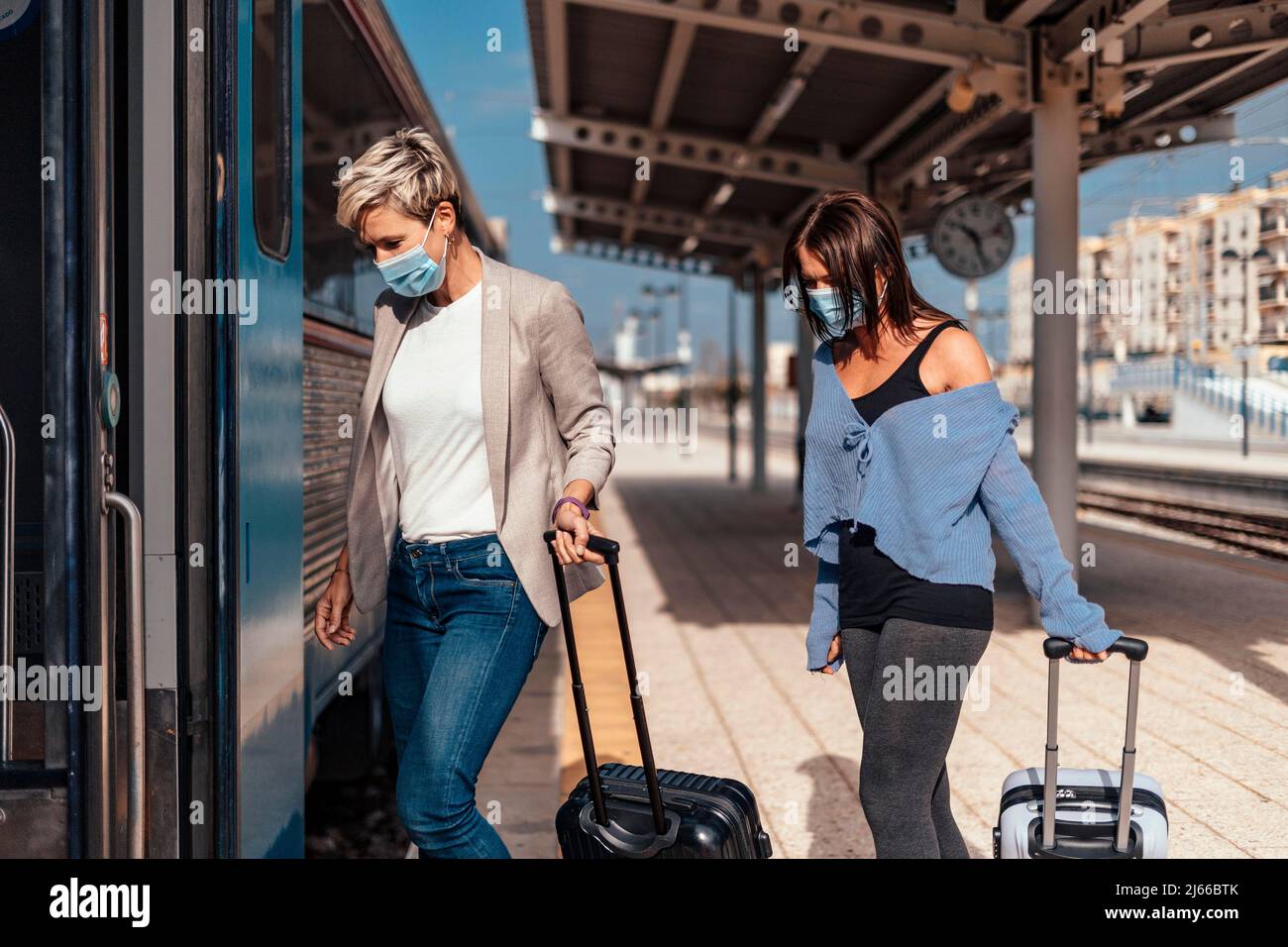 Due donne in maschere protettive salire sul treno con i bagagli Foto Stock