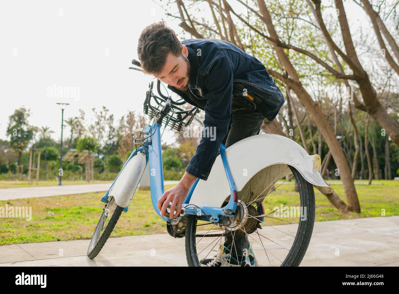 Il giovane uomo bello sta controllando la gomma sulla sua bici sul parco della città. Foto Stock