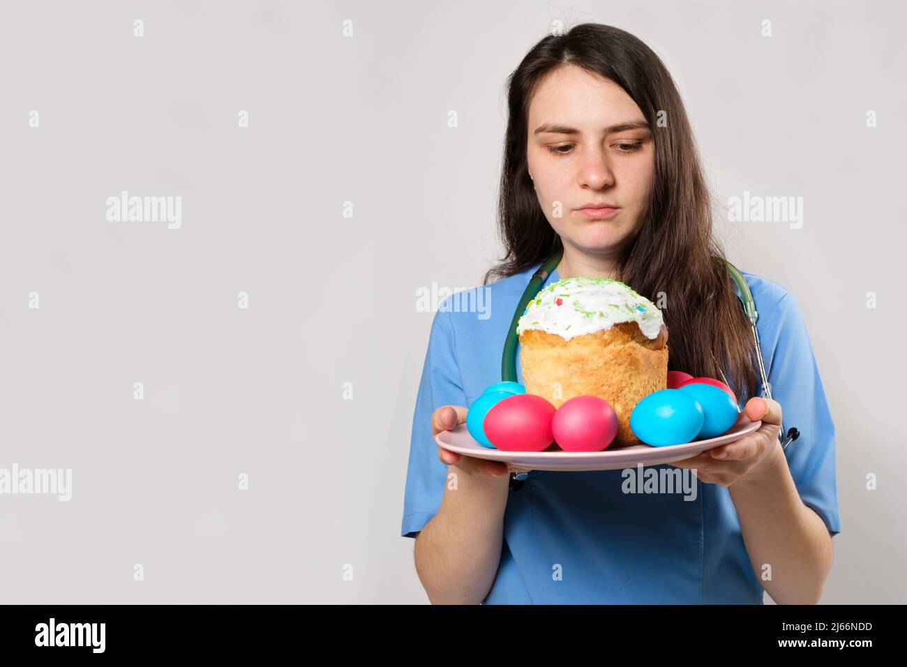 Un operatore medico in uniforme blu tiene una torta di Pasqua e le uova dipinte su uno sfondo bianco, un luogo per il testo. Foto Stock