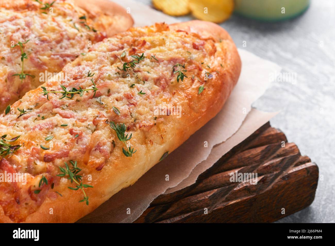 Barche Baguette. Sandwich caldo al forno su pane baguette con prosciutto, pancetta, verdure e formaggio su pergamena e legno stand su sfondo grigio cemento. Foto Stock